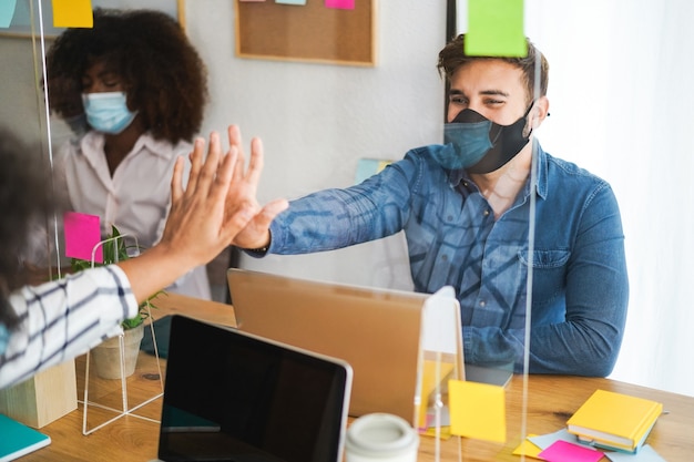 Foto jóvenes que trabajan dentro de un coworking detrás de plexiglás de seguridad durante el brote de coronavirus