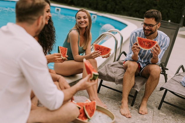 Jóvenes sentados junto a la piscina y comiendo sandía en el patio trasero de la casa