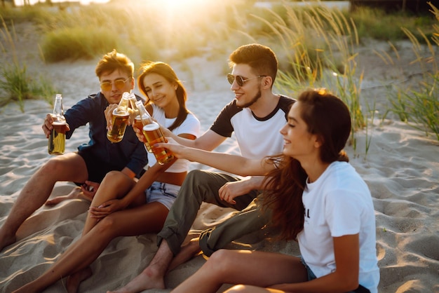 Jóvenes sentados juntos en la playa bebiendo cerveza Un grupo de amigos aclama con cervezas en la playa