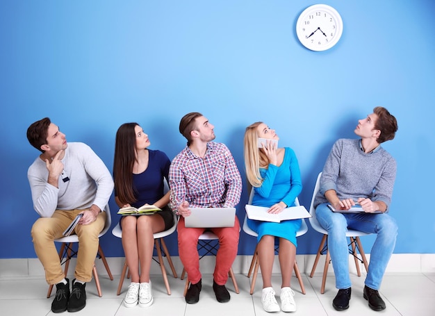 Jóvenes sentados en sillas y mirando el reloj en el salón azul