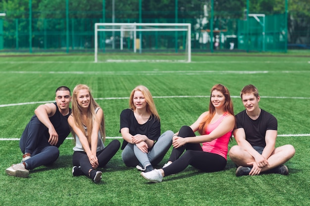 Los jóvenes se sientan en la hierba en el campo de fútbol.