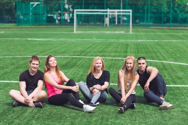 Los jóvenes se sientan en la hierba en el campo de fútbol.