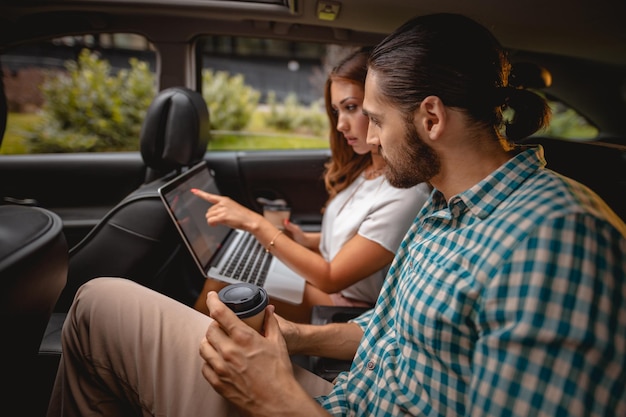 Jóvenes socios comerciales de confianza que trabajan en un viaje de negocios en el asiento trasero del automóvil.