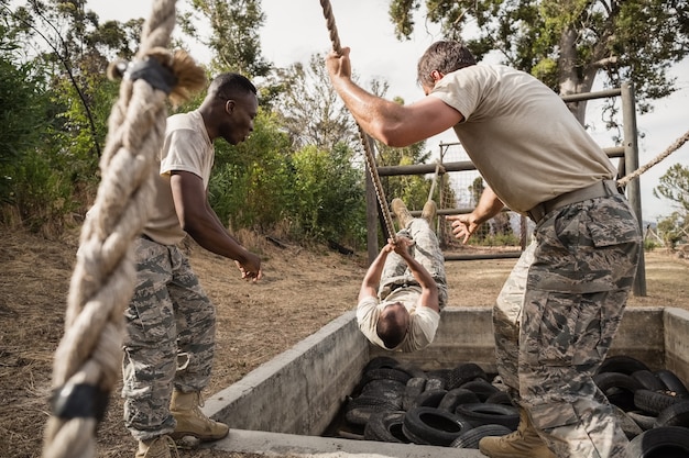 Jóvenes soldados militares practicando escalada en cuerda durante la carrera de obstáculos en el campo de entrenamiento