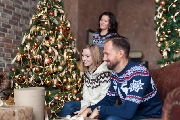 Los jóvenes sonriendo mientras están sentados cerca del árbol de Navidad con regalos de Navidad