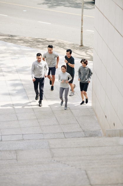 Jóvenes sonrientes hombres y mujeres vietnamitas trotar en la ciudad temprano en la mañana