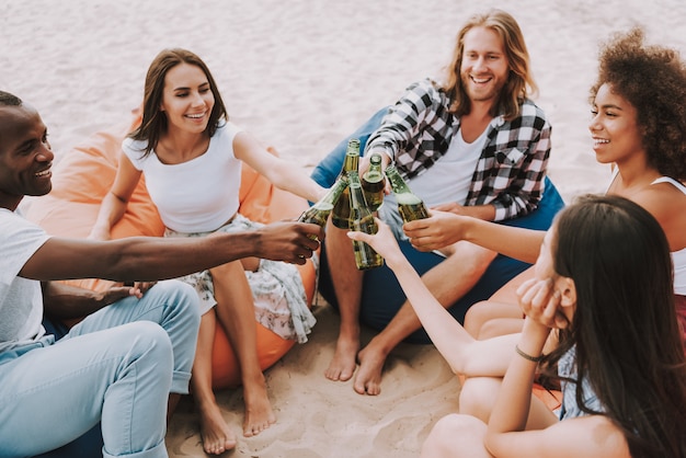 Los jóvenes tintinean botellas de cerveza en la playa