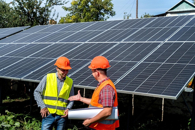 Jóvenes trabajadores uniformados con tabletas se dan la mano cerca de los nuevos paneles solares Concepto de electricidad verde