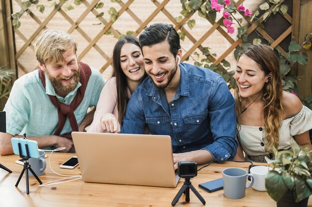 Los jóvenes transmiten en línea usando una computadora portátil y la cámara del teléfono móvil al aire libre en el restaurante