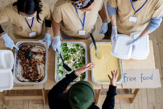 Jóvenes voluntarias dando recipientes con comida gratis a personas necesitadas