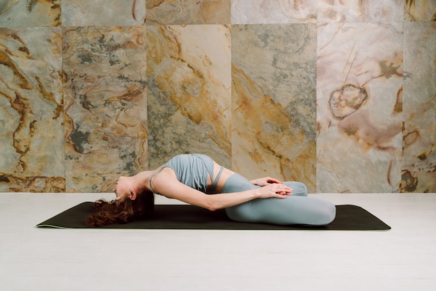 Jóvenes yoguis practicando Matsyasana posan en leggins azul pastel y top, enfoque selectivo