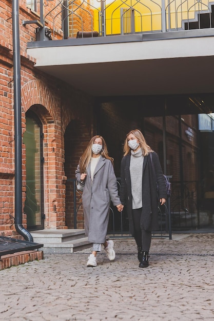 Jovens amigas bonitas com máscaras médicas se divertindo ao ar livre na noite de outono na cidade rindo e enlouquecendo o fim do conceito de pandemia