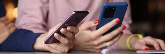 Jovens amigas estão sentadas à mesa com telefones celulares em close-up