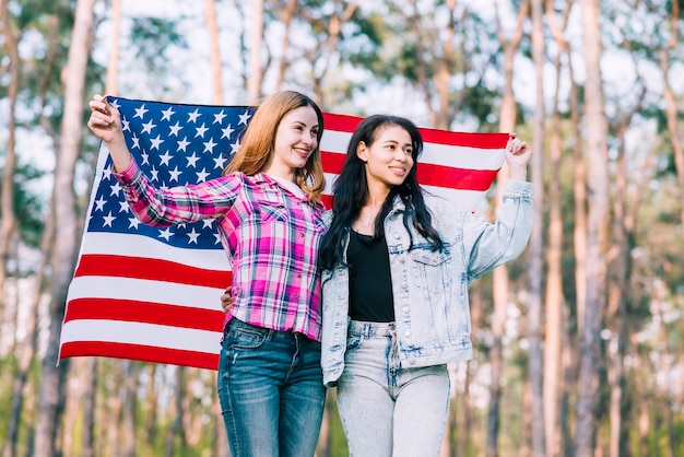 Jovens amigas felizes, abraçando e acenando a bandeira do EUA