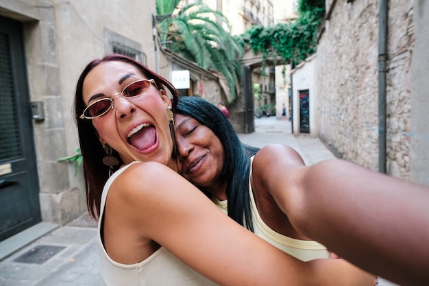 Jovens amigas se abraçando enquanto tiravam selfies juntos ao ar livre na rua. Conceito de amizade.