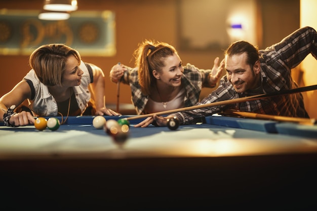 Foto jovens amigos alegres sorridentes estão jogando bilhar no bar depois do trabalho. eles estão envolvidos em atividades recreativas.