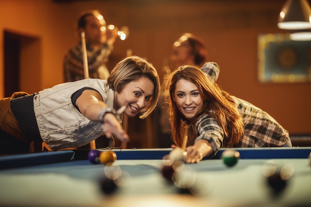 Foto jovens amigos alegres sorridentes estão jogando bilhar no bar depois do trabalho. eles estão envolvidos em atividades recreativas.