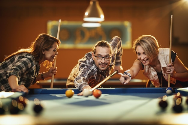 Jovens amigos alegres sorridentes estão jogando bilhar no bar depois do trabalho. Eles estão envolvidos em atividades recreativas.