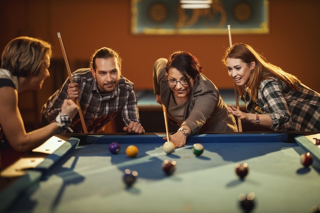 Jovens amigos alegres sorridentes estão jogando bilhar no bar depois do trabalho. Eles estão envolvidos em atividades recreativas.