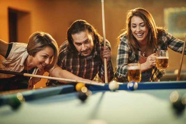 Jovens amigos alegres sorridentes estão jogando bilhar no bar depois do trabalho. Eles estão envolvidos em atividades recreativas.