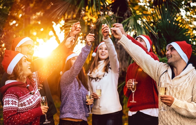 Foto jovens amigos com chapéu de papai noel comemorando o natal com brinde com vinho e champanhe ao ar livre