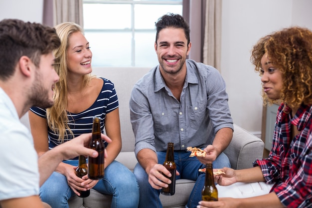 Jovens amigos desfrutando de cerveja e pizza no sofá em casa