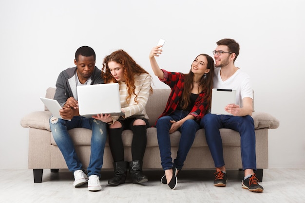 Jovens amigos fazendo selfie sentados no sofá e usando gadgets