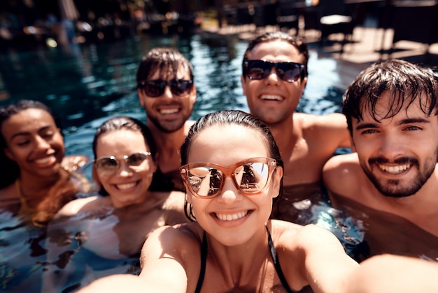 Jovens amigos felizes fazem selfie na piscina.