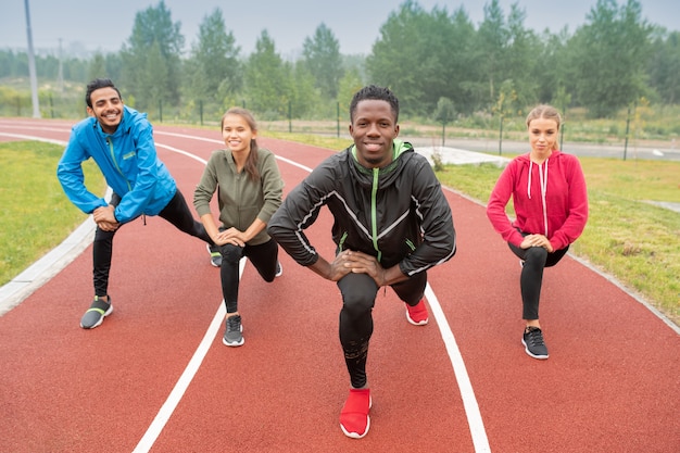 Jovens amigos interculturais saudáveis em roupas esportivas se exercitando nas pistas de corrida de um estádio ao ar livre durante o treino