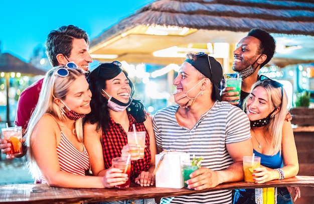 Jovens amigos internacionais conversando no bar de praia com máscara facial aberta