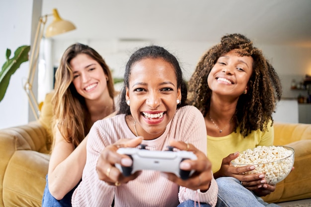 Jovens amigos jogam videogames juntos em casa apenas mulheres jogadores celebrando e comendo pipocas