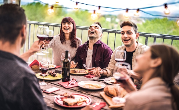 Jovens amigos se divertindo bebendo vinho tinto em um jantar na varanda da cobertura