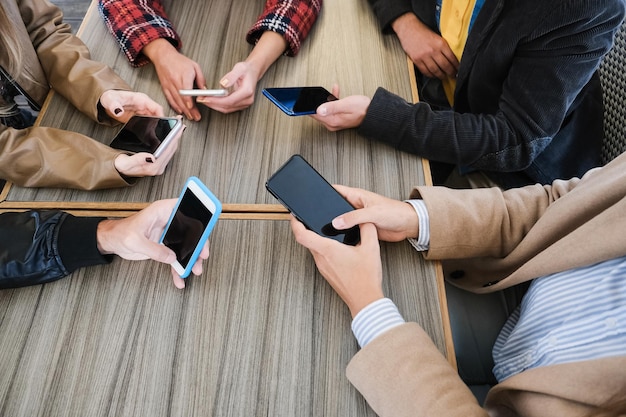 Jovens amigos se divertindo juntos usando telefones celulares - Foco principal nas mãos esquerdas segurando smartphone