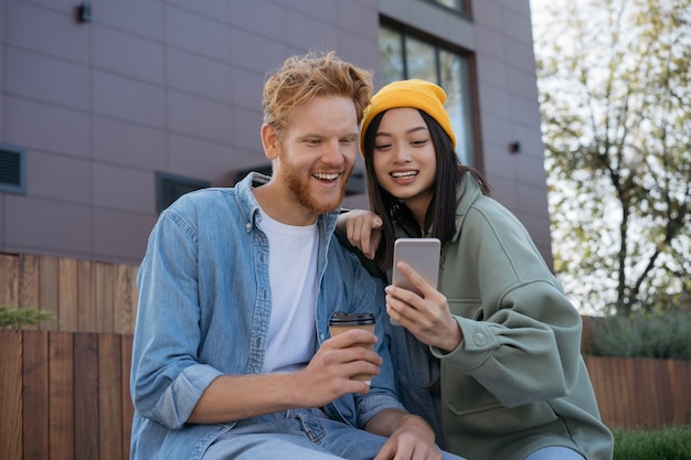 Jovens amigos sorridentes, usando o telefone celular, assistindo a vídeos de compras online