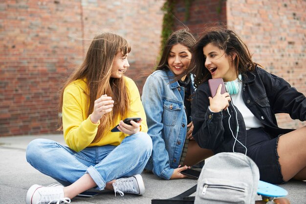 Foto jovens amigos usando o telefone enquanto estão sentados na rua