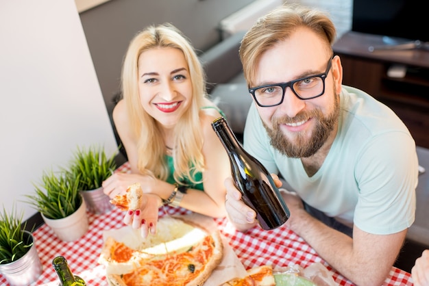 Jovens amigos vestidos casualmente com camisetas coloridas almoçando com pizza e cerveja em casa