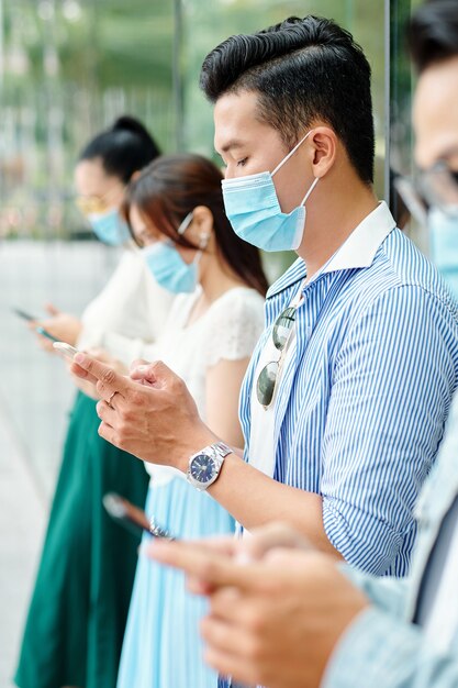 Jovens asiáticos ao ar livre com máscaras protetoras e usando aplicativos móveis em seus telefones para verificar as estatísticas de coronavírus