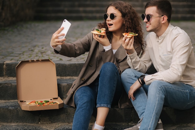 Jovens blogueiros fazem selfie com uma fatia de pizza nas mãos