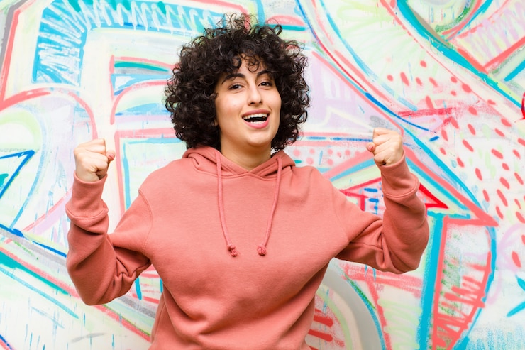 Foto jovens bonitas mulher afro, sentindo-se feliz surpreso e orgulhoso, gritando e comemorando o sucesso com um grande sorriso contra a parede do graffiti