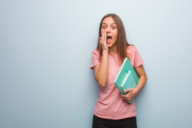 Jovens bonitas mulher caucasiana gritando algo feliz para a frente. Ela está segurando livros.