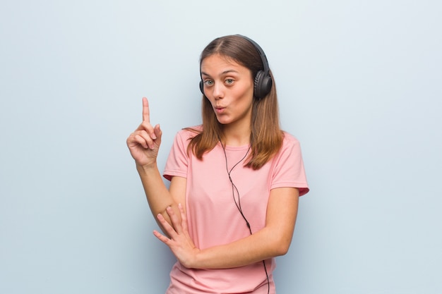 Foto jovens bonitas mulher caucasiana, tendo uma ótima idéia, criatividade. ela está ouvindo música com fones de ouvido.