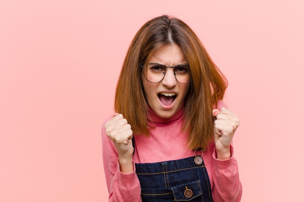 Jovens bonitas mulher gritando agressivamente com olhar irritado, frustrado, irritado e punhos apertados, sentindo-se furioso com rosa