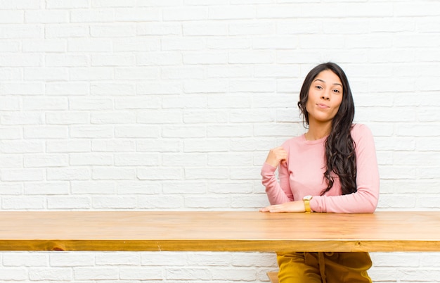 Jovens bonitas mulher latina olhando arrogante, bem sucedido, positivo e orgulhoso, apontando para si mesmo sentado na frente de uma mesa