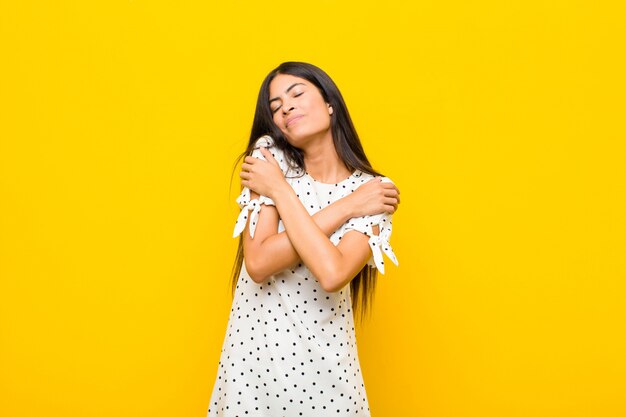 Jovens bonitas mulher latina se sentindo apaixonada, sorrindo, abraçando e abraçando a si mesma, permanecendo solteira, sendo egoísta e egocêntrica contra a parede plana