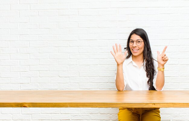 Jovens bonitas mulher latina sorrindo e olhando amigável, mostrando o número sete ou sétimo com a mão para a frente, contagem regressiva, sentado na frente de uma mesa