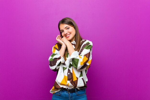 Jovens bonitas mulher se sentindo apaixonado e bonito, adorável e feliz, sorrindo romanticamente com as mãos ao lado do rosto contra roxo