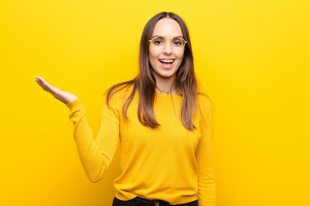 Jovens bonitas mulher se sentindo feliz, surpreso e alegre, sorrindo com atitude positiva, percebendo uma solução ou idéia sobre parede laranja