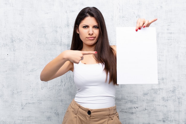 Jovens bonitas mulher segurando uma folha de papel contra a parede de cimento grunge