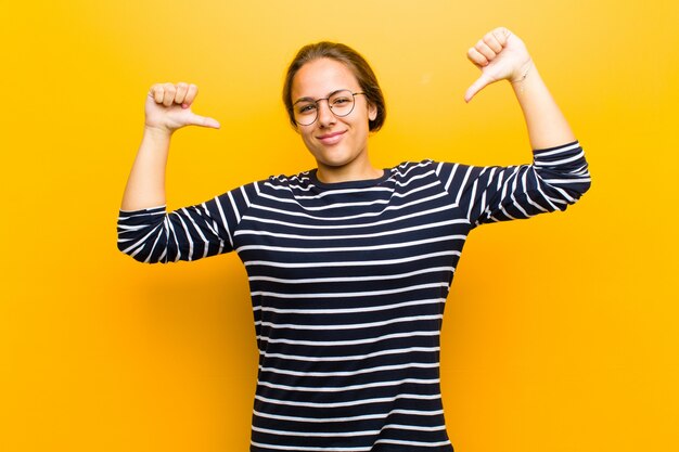 Jovens bonitas mulher sentindo-se orgulhoso, arrogante e confiante, parecendo satisfeito e bem-sucedido, apontando para si mesmo contra a laranja