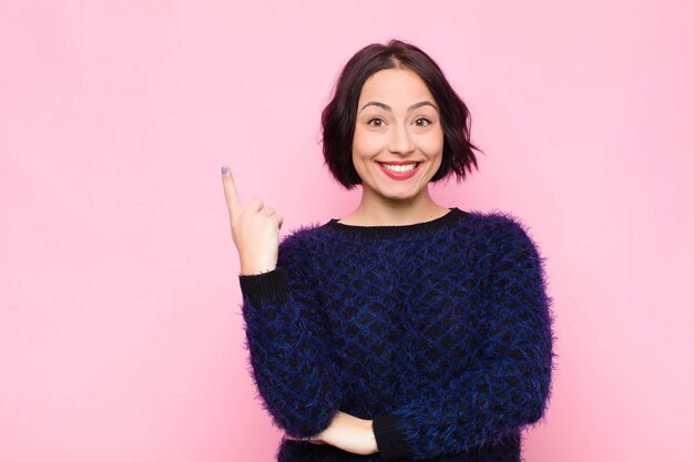 Jovens bonitas mulher sorrindo alegremente e olhando de soslaio, pensando, pensando ou tendo uma idéia contra parede rosa